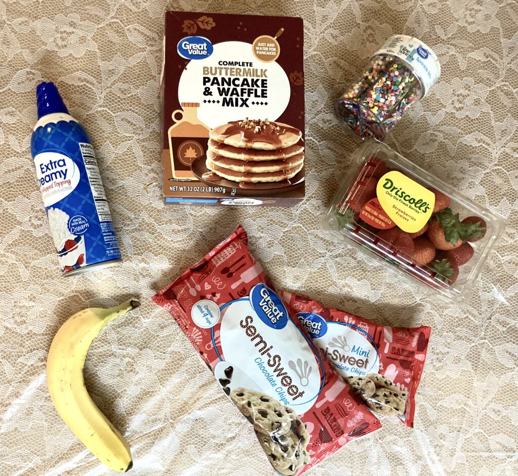 Ingredients, including pancake mix, strawberries, bananas, whipped cream, chocolate chips, and sprinkles.
