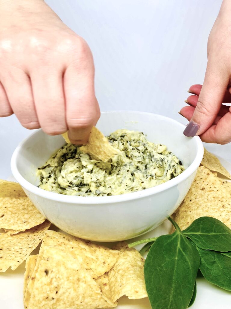 A chip being dipped into a bowl of Instant Pot spinach artichoke dip