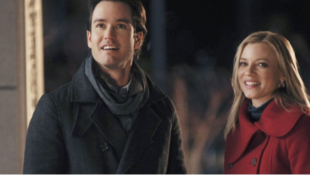 A man and a woman in a red coat play in the snow in the holiday romance movie the 12 Dates of Christmas, streaming on Disney Plus