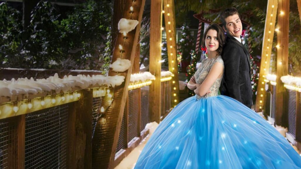 A boy and girl in a fancy blue ball gown stand back to back on a snowy bridge with lights around in the holiday chick flick A Cinderella Story: Christmas Wish