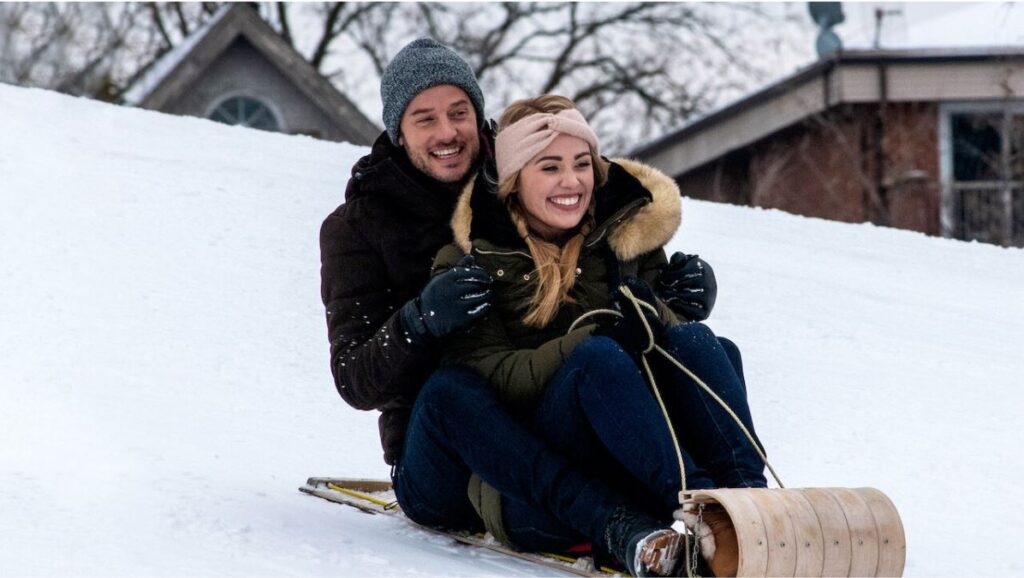 Two young adults sled down a hill of snow together in the holiday chick flick Midnight at the Magnolia