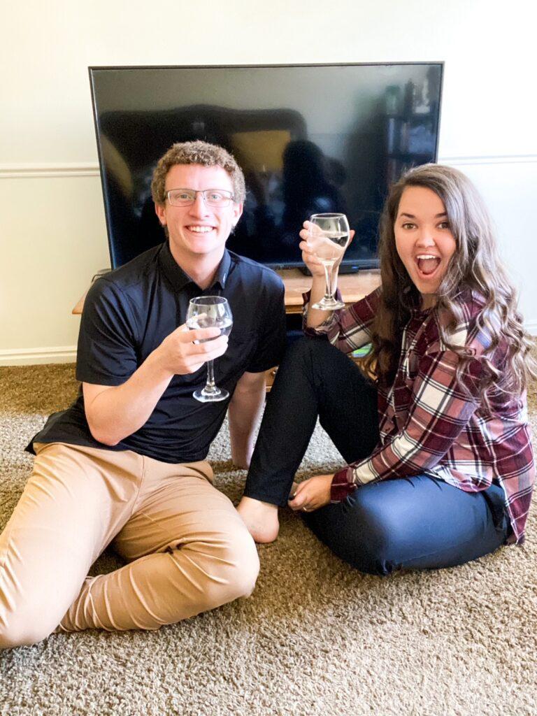Smiling Couple holds glasses in front of a tv