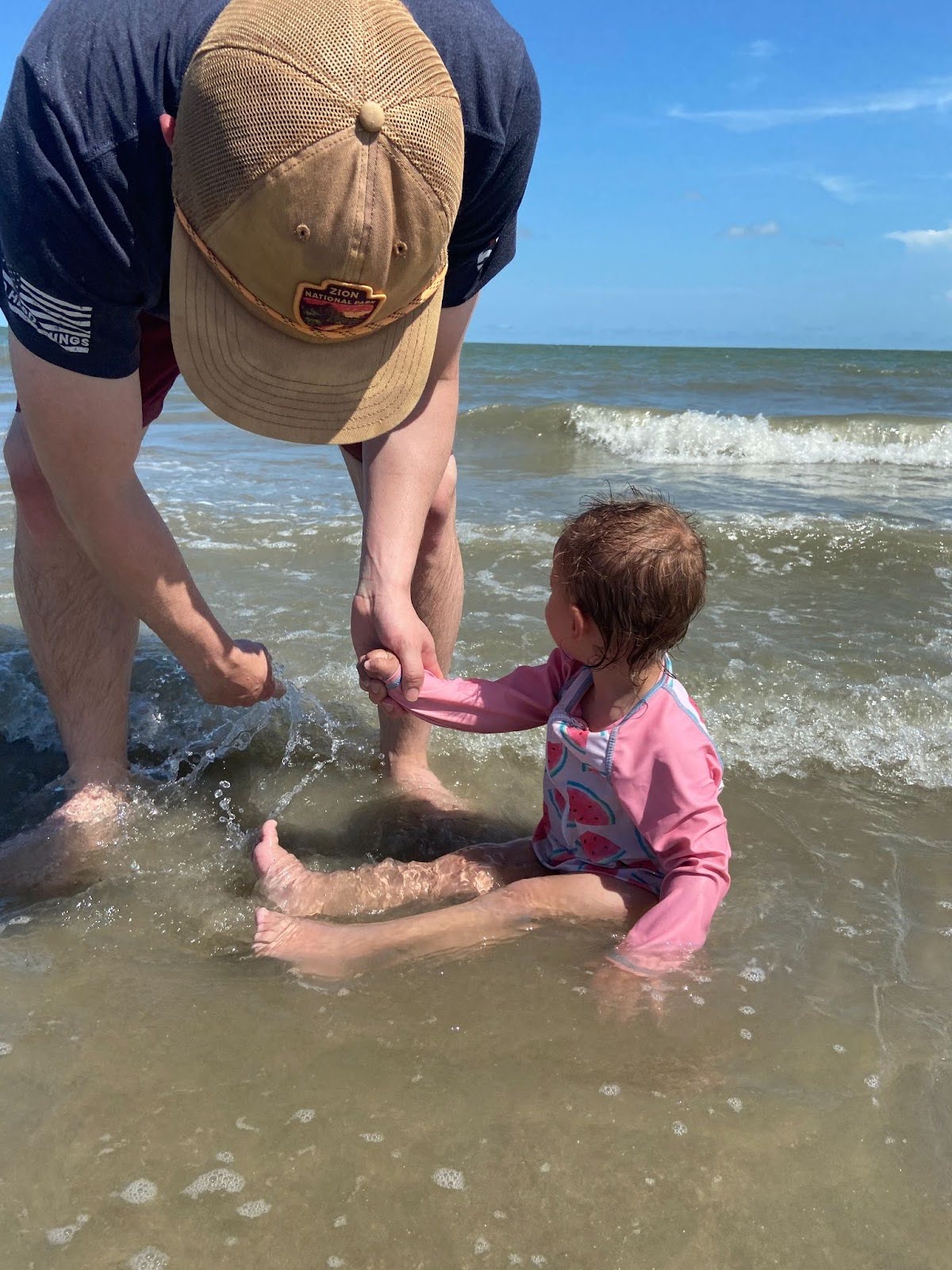 toddler plays in shallow beach water with her father