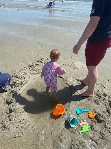 toddler plays in shallow dug pool at the beach with her father